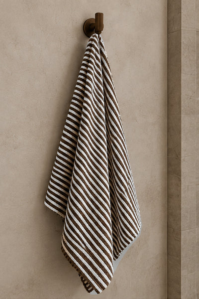 Brown and white striped bath towel hanging from a brass bathroom wall hook.