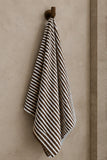 Brown and white striped bath towel hanging from a brass bathroom wall hook.