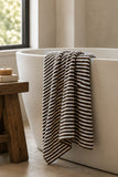 Brown and white striped bath towel draped over a freestanding white bathtub.