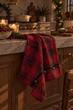 Red tartan holiday kitchen towel with three sewn bells styled in a warm Christmas kitchen